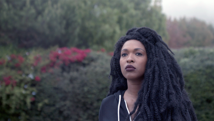 Film still from THE TUBA THIEVES: A young woman stands in the greenery and gazes into the distance.