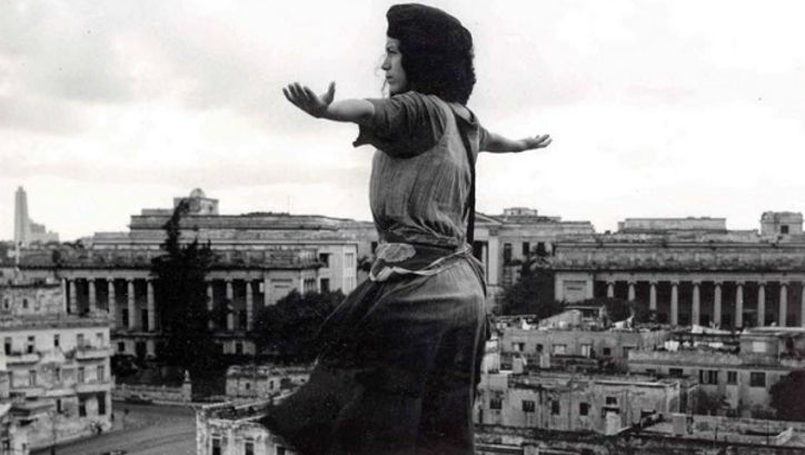 Film still from MADAGASCAR: A young woman stands with outstretched arms above the rooftops of a city.