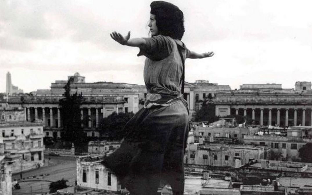 Film still from MADAGASCAR: A young woman stands with outstretched arms above the rooftops of a city.
