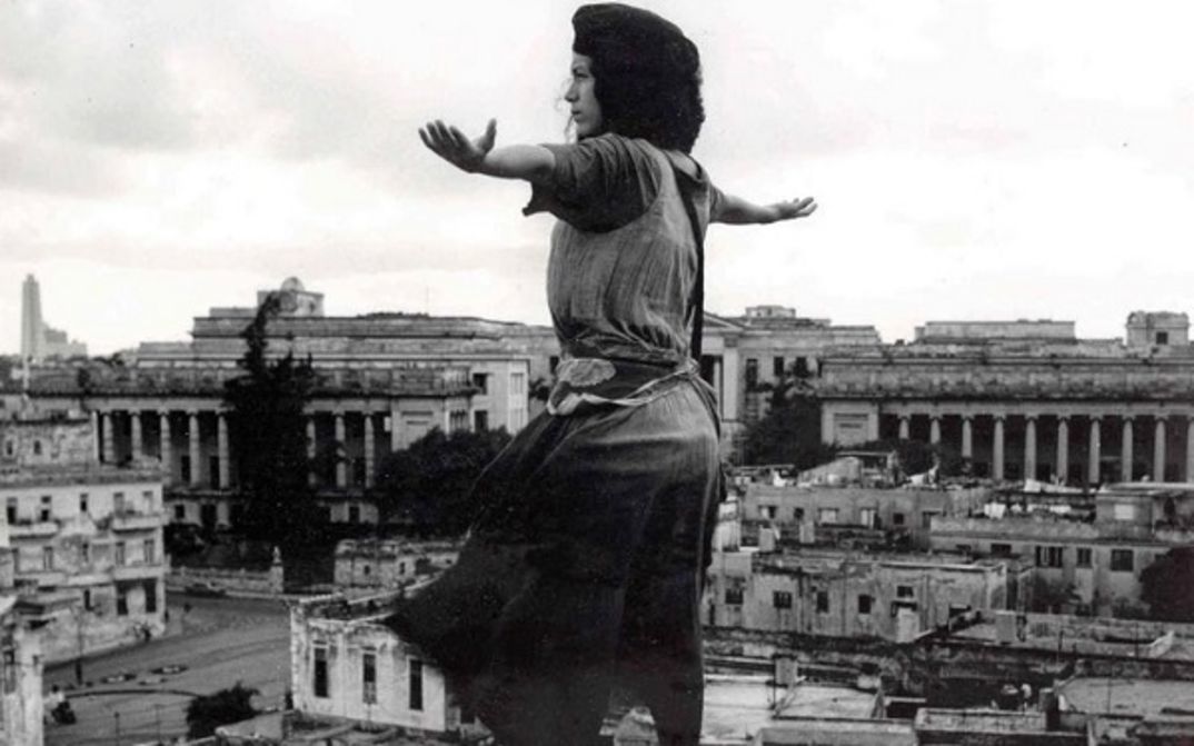 Film still from MADAGASCAR: A young woman stands with outstretched arms above the rooftops of a city.