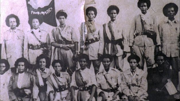 Historical group photo of several women in uniform, some standing and some seated, in front of a banner.