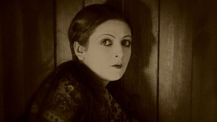Film still from VARIETÉ: A woman stands at a door and turns to face the camera.