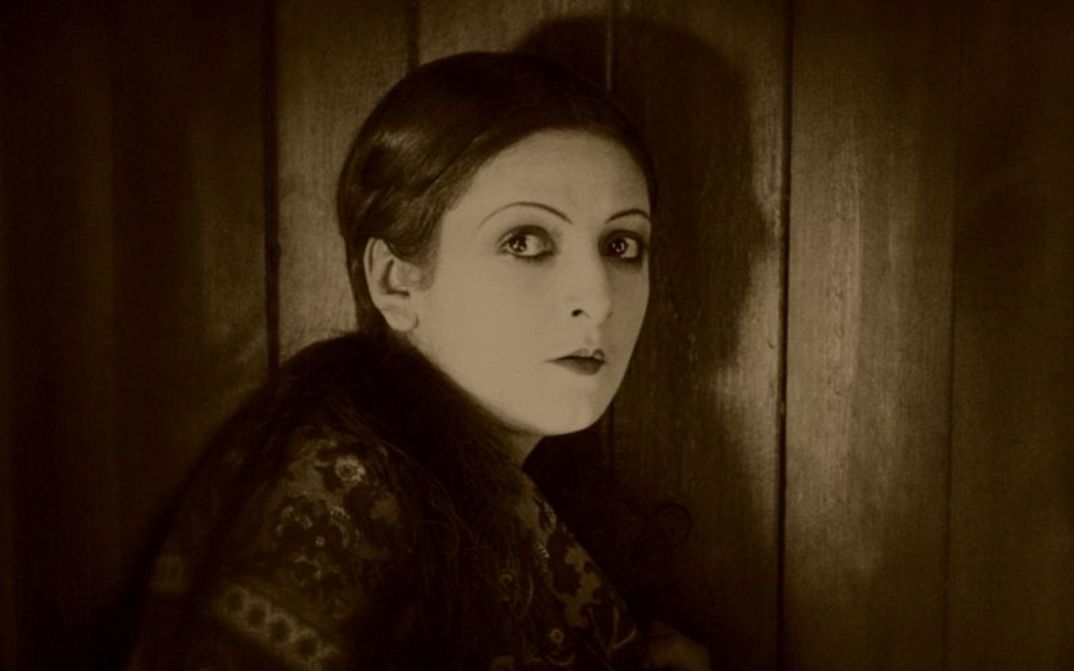Filmstill aus VARIETÉ: Eine Frau steht an einer Tür und dreht sich zur Kamera um.
