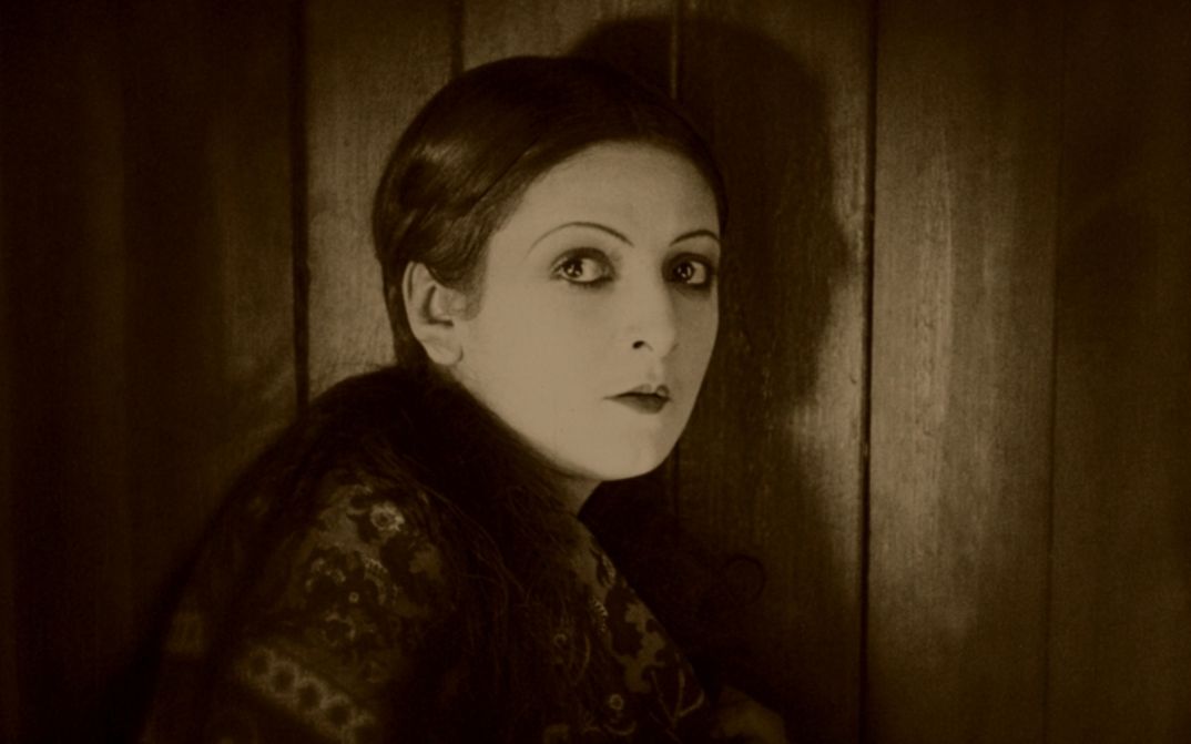 Filmstill aus VARIETÉ: Eine Frau steht an einer Tür und dreht sich zur Kamera um.