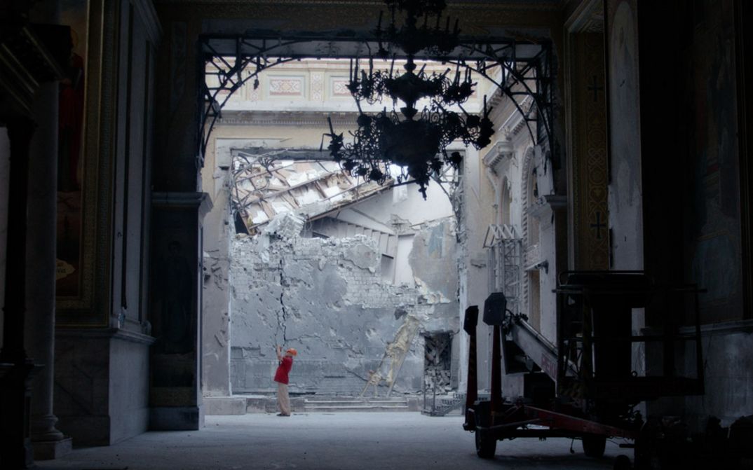 We are standing in a passageway and can see a damaged wall in the background. A man is standing at the back taking photographs.