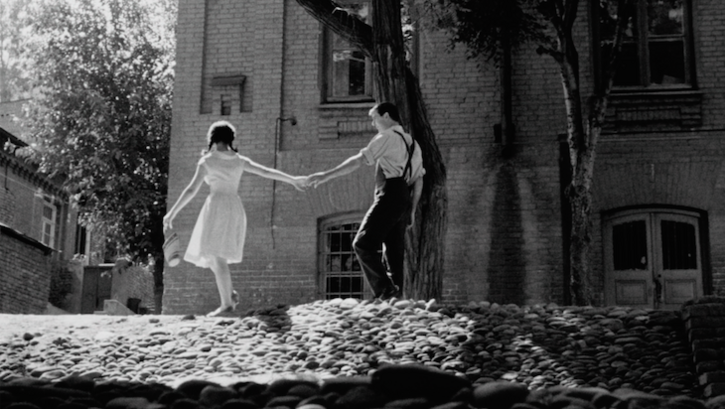 Film still from APRILI: Two young people hold hands on a cobbled street.
