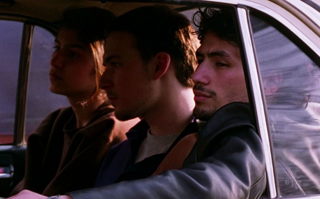 Filmstill aus GESCHWISTER: Drei junge Menschen sitzen bei offenem Fenster auf der Rückbank im Auto.