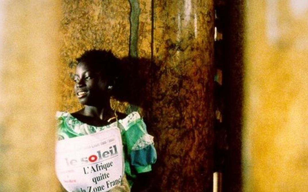 Filmstill aus LA PETITE VENDEUSE DE SOLEIL: Ein Mädchen steht mit einer Ausgabe der Zeitung "Le Soleil" an einer Ecke.