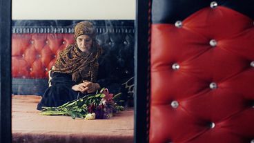 Filmstill from "Anqa" by Helin Çelik. A veiled woman sits meditatively in front of a bouquet of flowers.