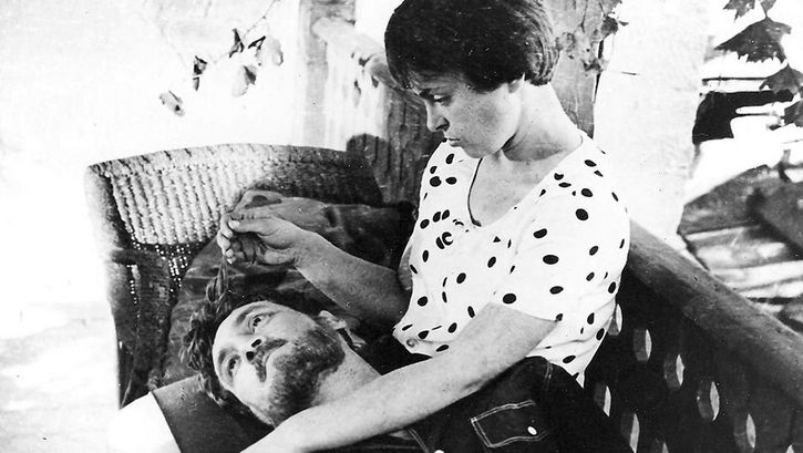 Film still from BRIEF ENCOUNTERS: A woman and a man on a bench, he has his head in her lap, she is stroking his hair.