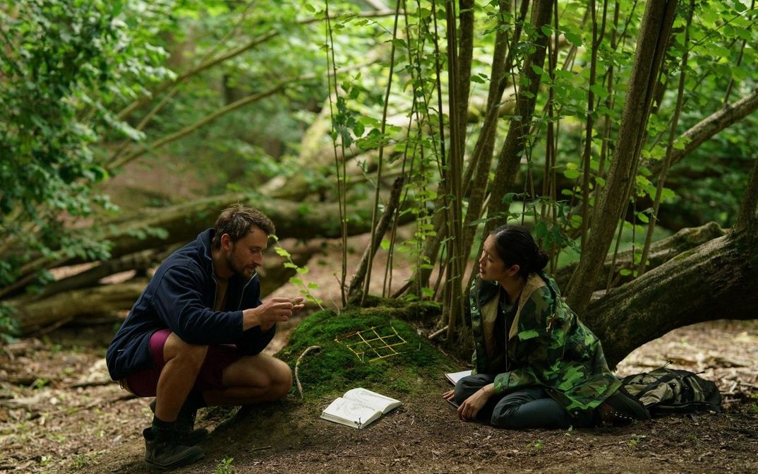 Filmstill aus HERE: Zwei Menschen sitzen auf dem Waldboden und betrachten das Moos zwischen ihnen.