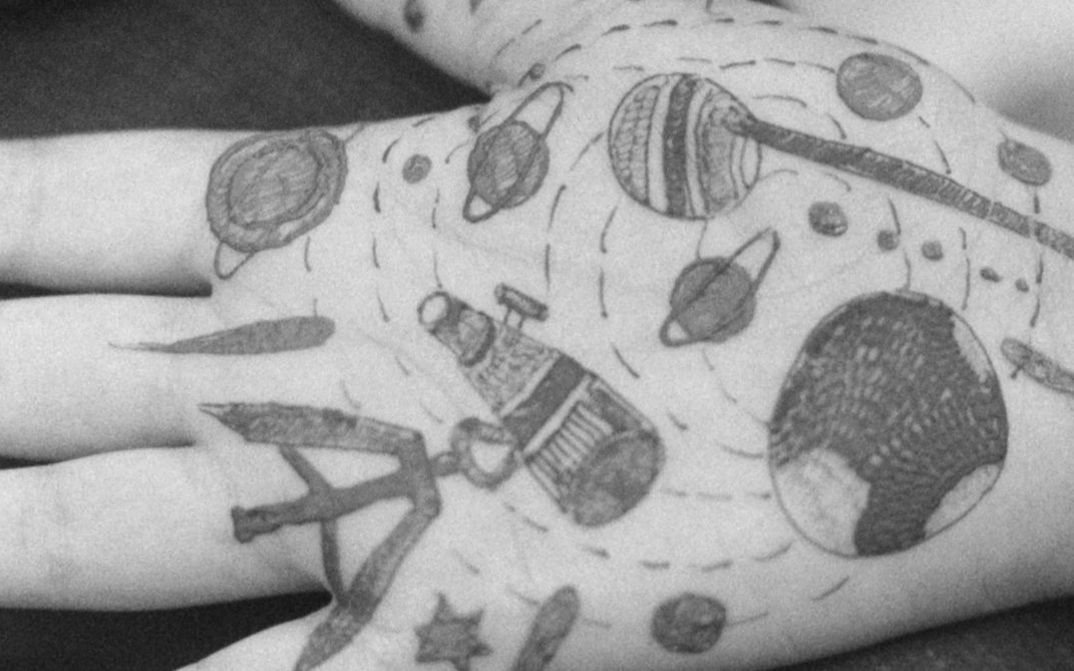 Film still from Gavati Wad’s film “O Seeker”. The palm of a hand with various illustrations drawn onto it, including planets, stars, and lines.