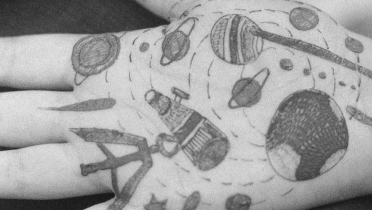 Film still from Gavati Wad’s film “O Seeker”. The palm of a hand with various illustrations drawn onto it, including planets, stars, and lines. 