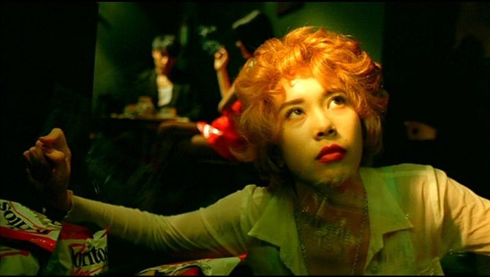 Film still from FALLEN ANGELS: Close-up of a young woman with reddish-blond curls. She looks upwards, behind her people can be seen in a bar. 