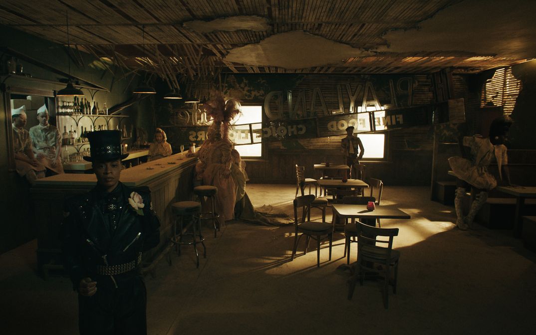 Filmstill aus PLAYLAND: Eine Reihe von Menschen in fantasievollen Kostümen stehen in einer sonst leeren Bar.