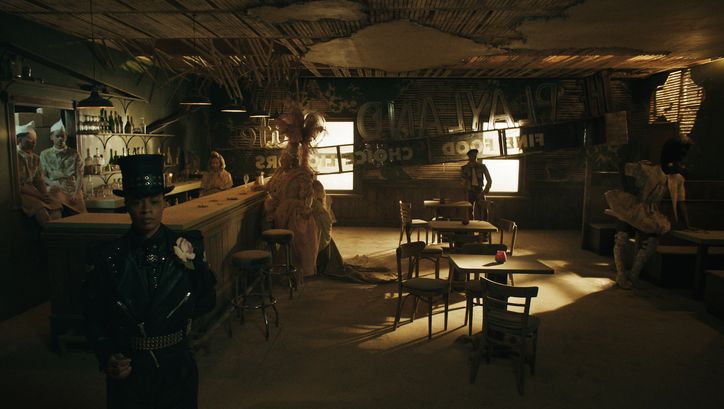 Filmstill aus PLAYLAND: Eine Reihe von Menschen in fantasievollen Kostümen stehen in einer sonst leeren Bar.