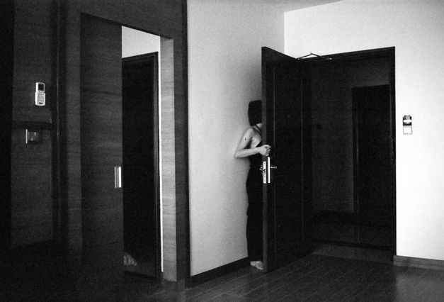 Still from the film "Jet Lag" by Zheng Lu Xinyuan. A black-and-white image of a girl hiding behind an open hotel room door, with the side of her body and her hair visible.