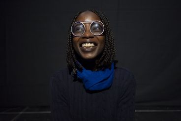 A portrait of the artist, she wears large glasses and laughs at the camera. 