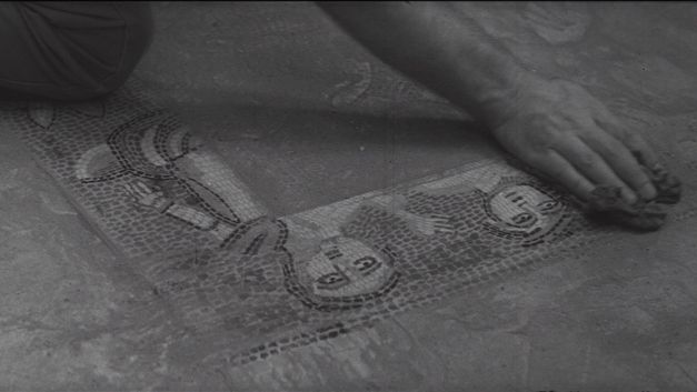 Film still from MES FANTÔMES ARMENIENS by Tamara Stepanyan. The black-and-white image shows a hand with a cloth wiping the floor tiles. 