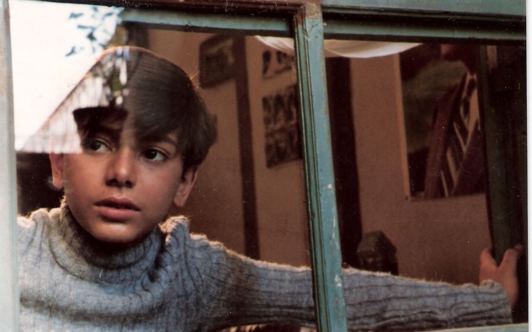 Film still from DREAMS OF THE CITY: A boy looks through a window to the outside.