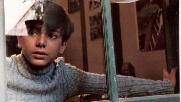 Film still from DREAMS OF THE CITY: A boy looks through a window to the outside.