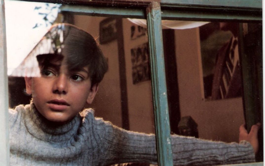 Film still from DREAMS OF THE CITY: A boy looks through a window to the outside.