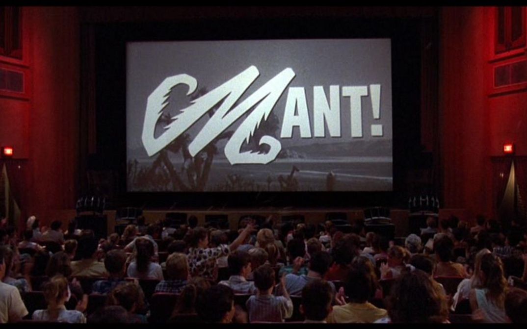 Film still from MATINEE: You see a crowded cinema hall, a black and white film is shown on the screen.