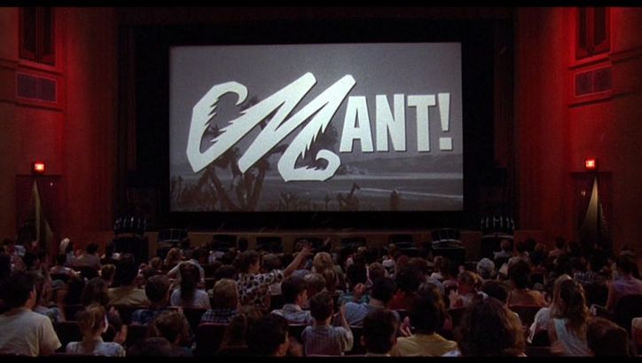 Film still from MATINEE: You see a crowded cinema hall, a black and white film is shown on the screen.