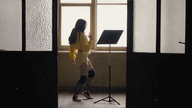 Still from the film "If Revolution Is a Sickness" by Diane Severin Nguyen. A woman dances in front of a music stand.