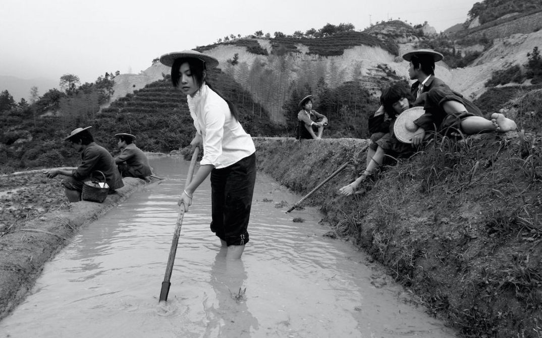 Film still from SEVEN INTELLECTUALS IN A BAMBOO FOREST: Some people are working and sitting in a terraced rice field.
