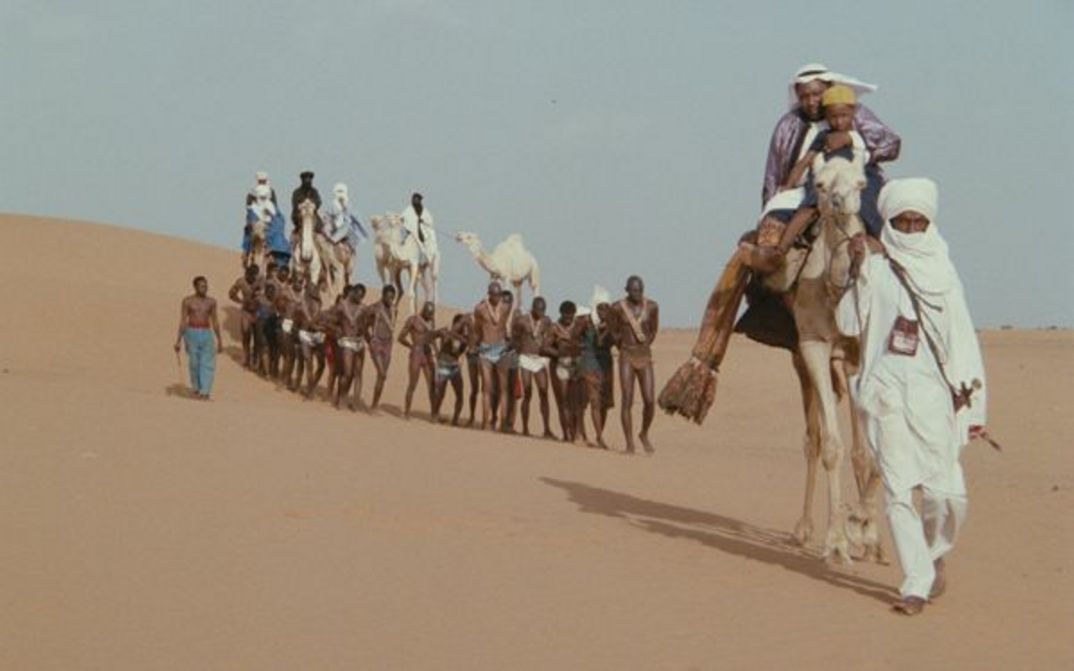 Filmstill aus SHAIHU UMAR: Eine Karawane in der Wüste. In der Mitte sind Menschen, die gefangen geworden sind.