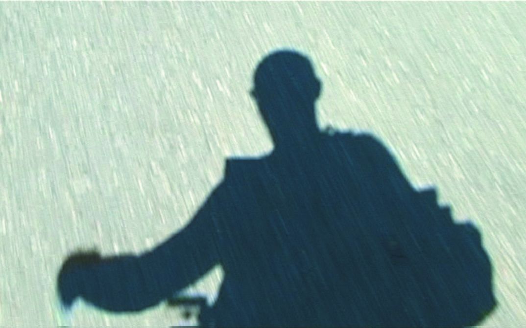 Filmstill aus HANS IM GLÜCK: Auf dem flirrenden Asphalt sieht man den Schatten einer Person.