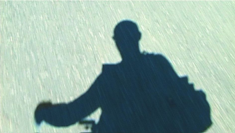 Filmstill aus HANS IM GLÜCK: Auf dem flirrenden Asphalt sieht man den Schatten einer Person.