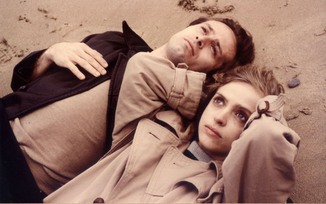 Film still from FLUCHT IN DEN NORDEN. A man and a woman lie in the sand and look up to the sky.