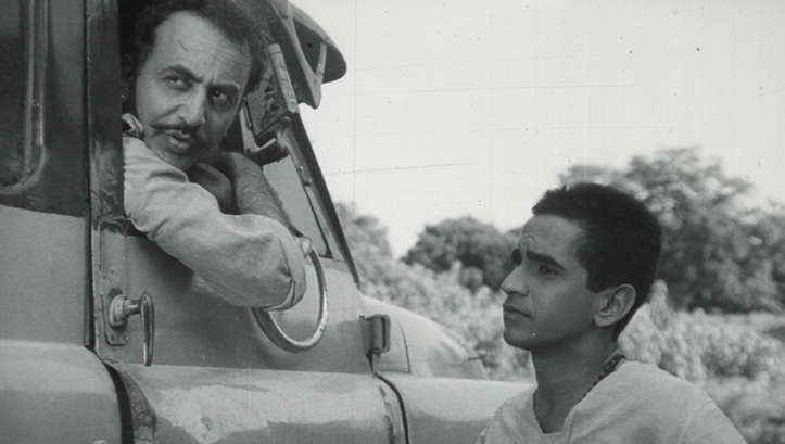 Film still from BADNAM BASTI: Two men talking, one sitting in a truck, the other standing in the street.