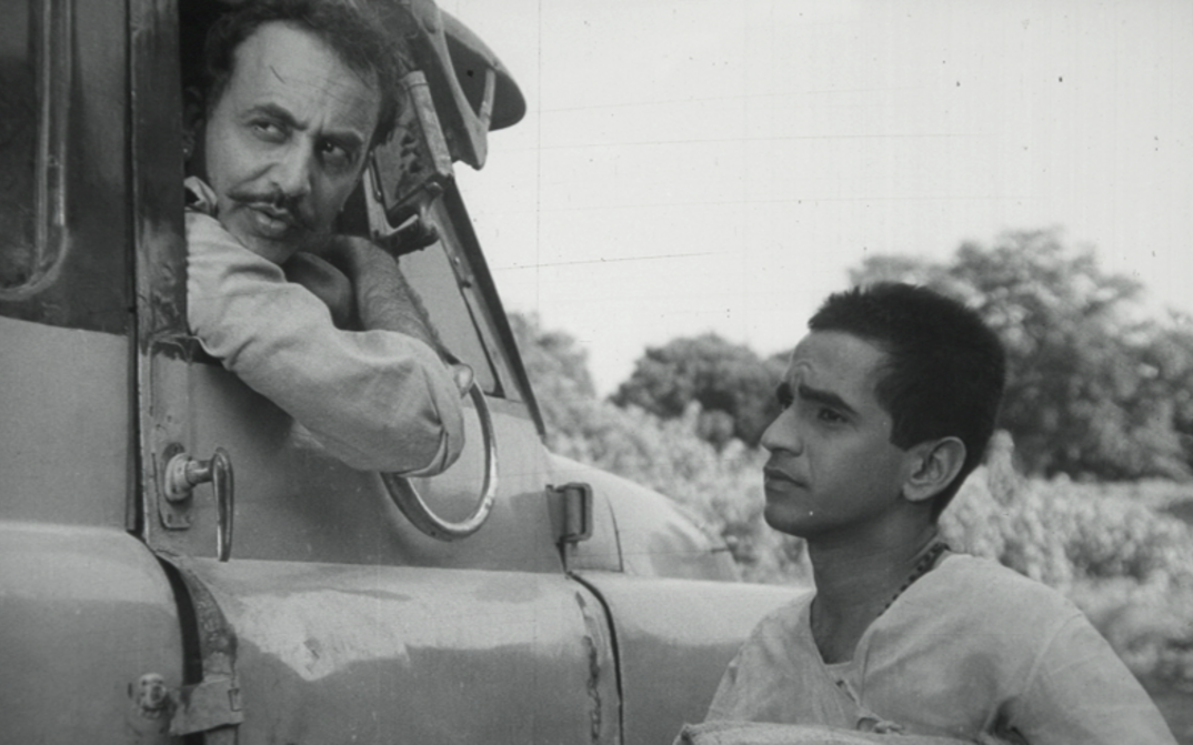 Filmstill aus BADNAM BASTI: Zwei Männer im Gespräch, einer sitzt in einem Lastwagen, der andere steht auf der Straße.