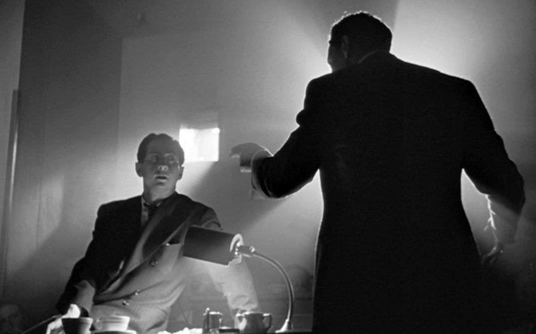 Filmstill aus CITIZEN KANE: Zwei Männer stehen diskutierend an einem Schreibtisch. Von einem der Männer sieht man nur den Rücken.