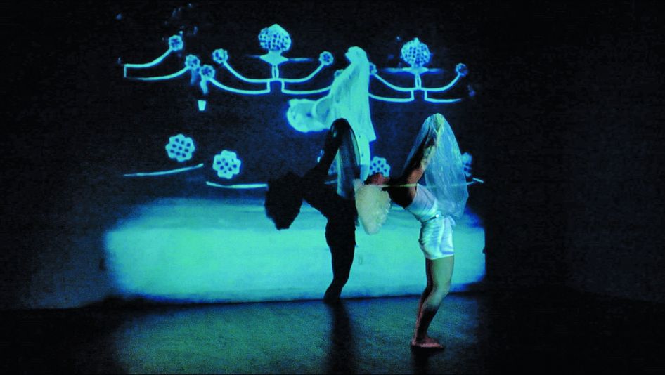 Film still from SALOMANIA: A person dances in front of colorful images projected on the wall.