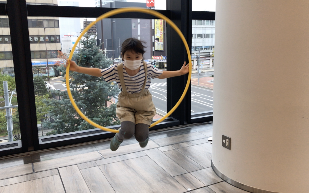 Filmstill aus HOOP LOOP: Ein japanisches Kind mit einer Gesichtsmaske spielt mit einem Hula-Hoop-Reifen.