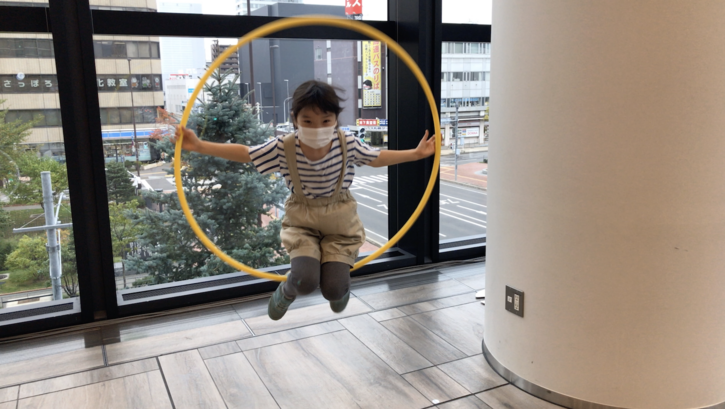 Filmstill aus HOOP LOOP: Ein japanisches Kind mit einer Gesichtsmaske spielt mit einem Hula-Hoop-Reifen.