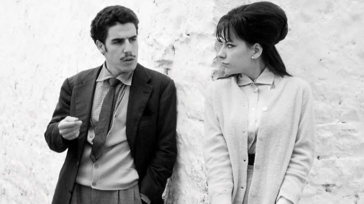 Film still from I BASILISCHI: A man and a woman look at each other leaning against a wall.