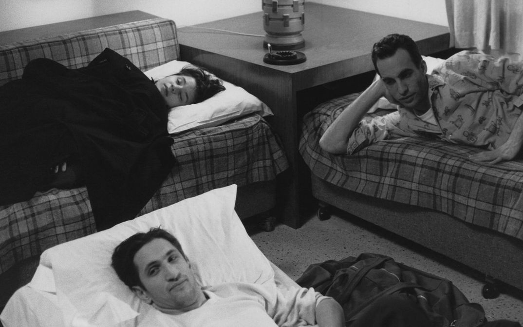 Filmstill aus STRANGER THAN PARADISE: Zwei Männer und eine Frau liegen in einem Zimmer in improvisierten Betten.