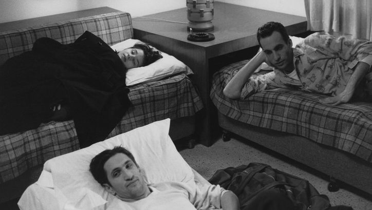 Filmstill aus STRANGER THAN PARADISE: Zwei Männer und eine Frau liegen in einem Zimmer in improvisierten Betten.