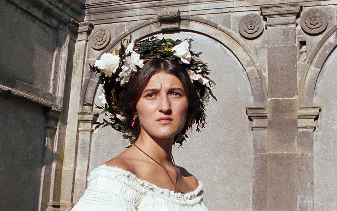 Filmstill aus RE GRANCHIO. Eine Frau in einem weißen Kleid und Blumen im Haar schaut stirnrunzelnd in die Ferne.
