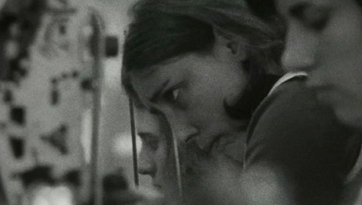 Film still from ES KOMT DRAUF AN, SIE ZU VERÄNDERN: You can see the heads of some young women; they work in a factory.