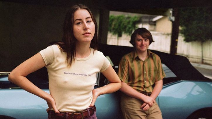 Film still from LICORICE PIZZA: A young woman looks into the camera. Behind her a teenager looks at her.