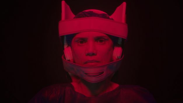 Frau blickt frontal in die Kamera und trägt einen technischen Helm, beleuchtet von rotem Licht.