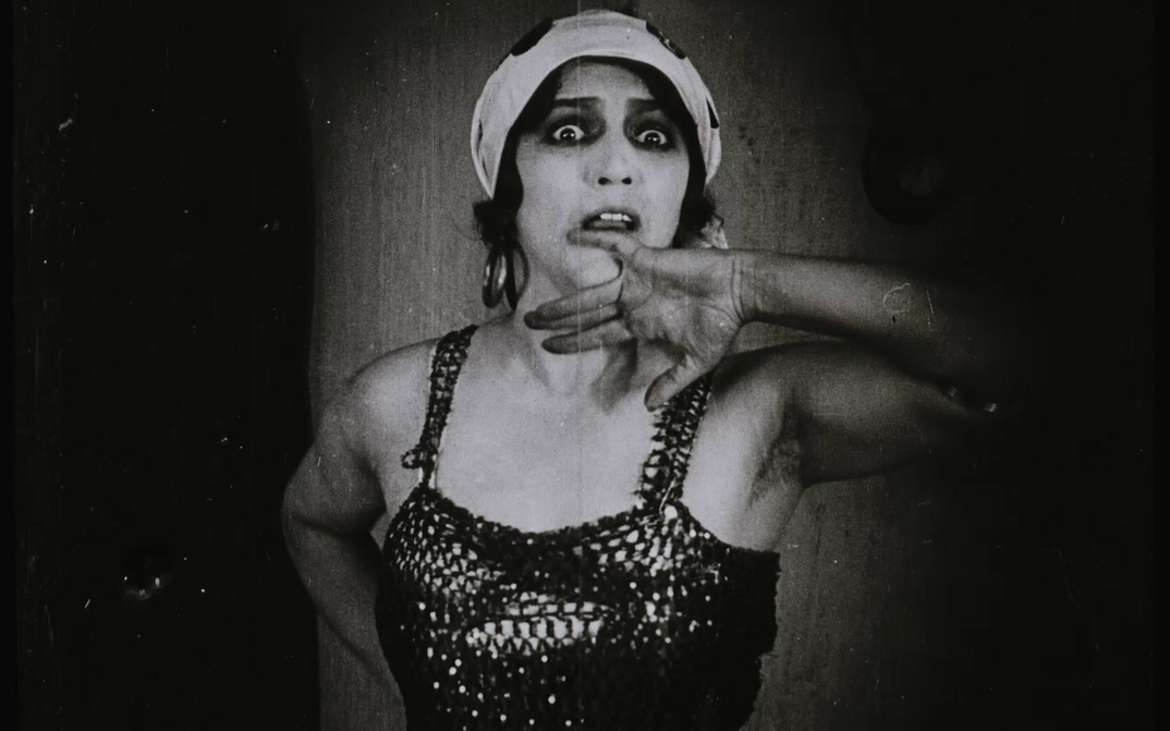 Film still from ABERGLAUBE: A woman looks startled and holds her hand to her face.