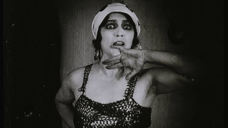 Film still from ABERGLAUBE: A woman looks startled and holds her hand to her face.