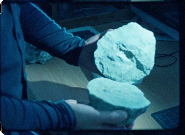 Film still from Ana Vaz’s film “A árvore”. A split stone is presented over a wooden table.